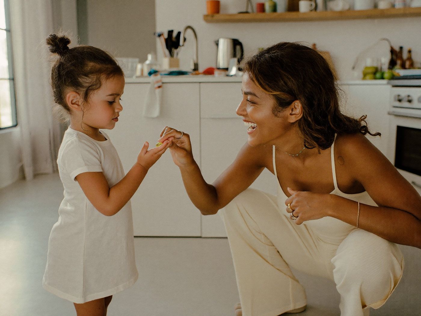 A mother handing her young child a gummy vitamin in the kitchen during their morning routine