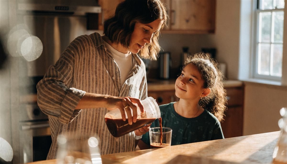 A mother pouring a chocolate protein shake for her daughter in their kitchen